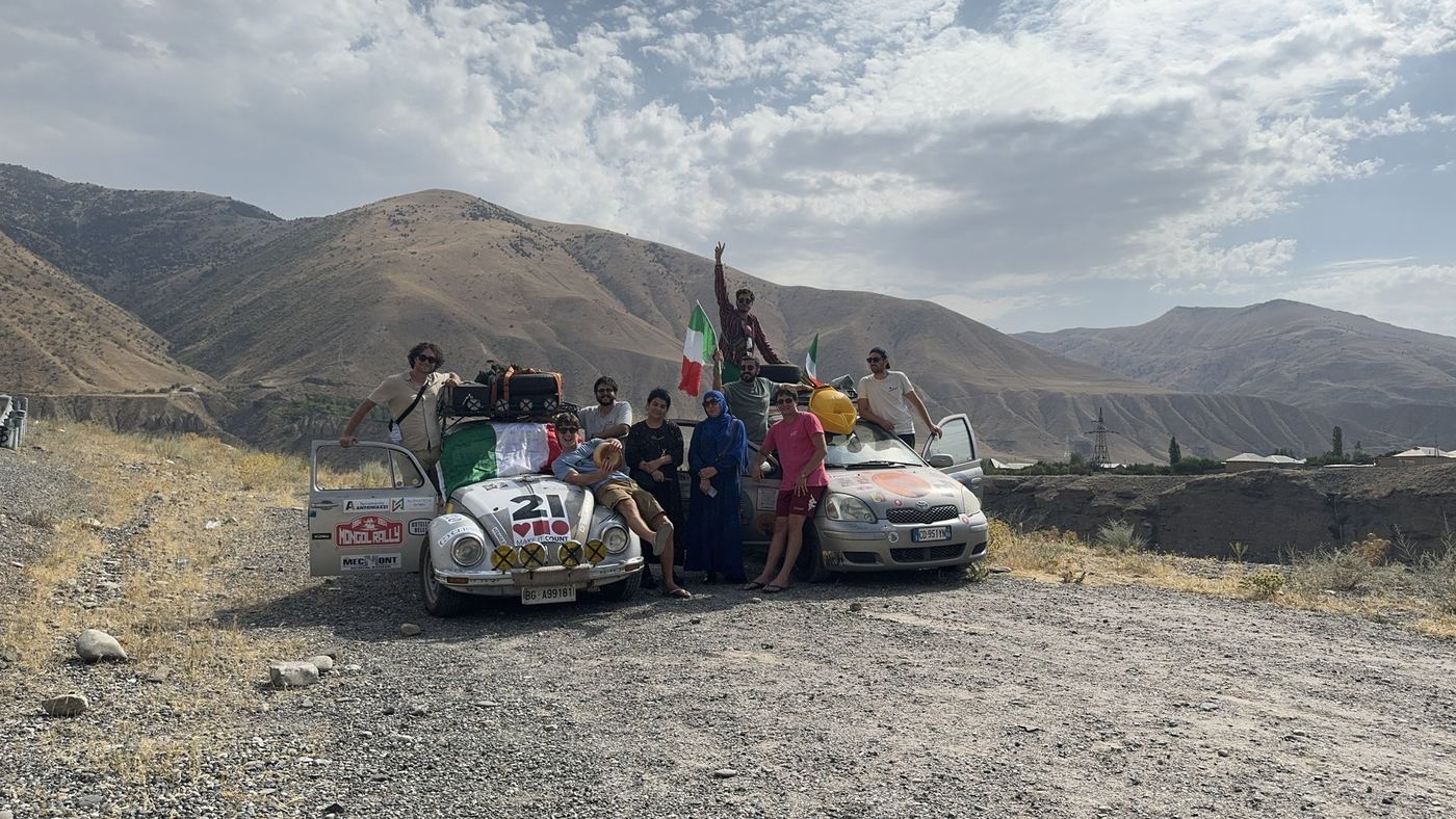 Il team con due auto del rally e la bandiera italiana, tra le montagne dell'Asia centrale